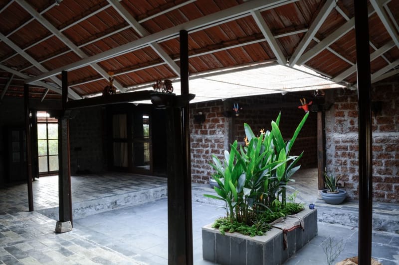 Open farmhouse courtyard with exposed brick walls, dark timber columns and a central planter under a clay-tiled roof