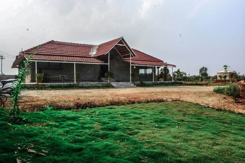 Single-storey Hyderabad farmhouse exterior with red clay-tile roof, exposed stone walls and a wide green lawn