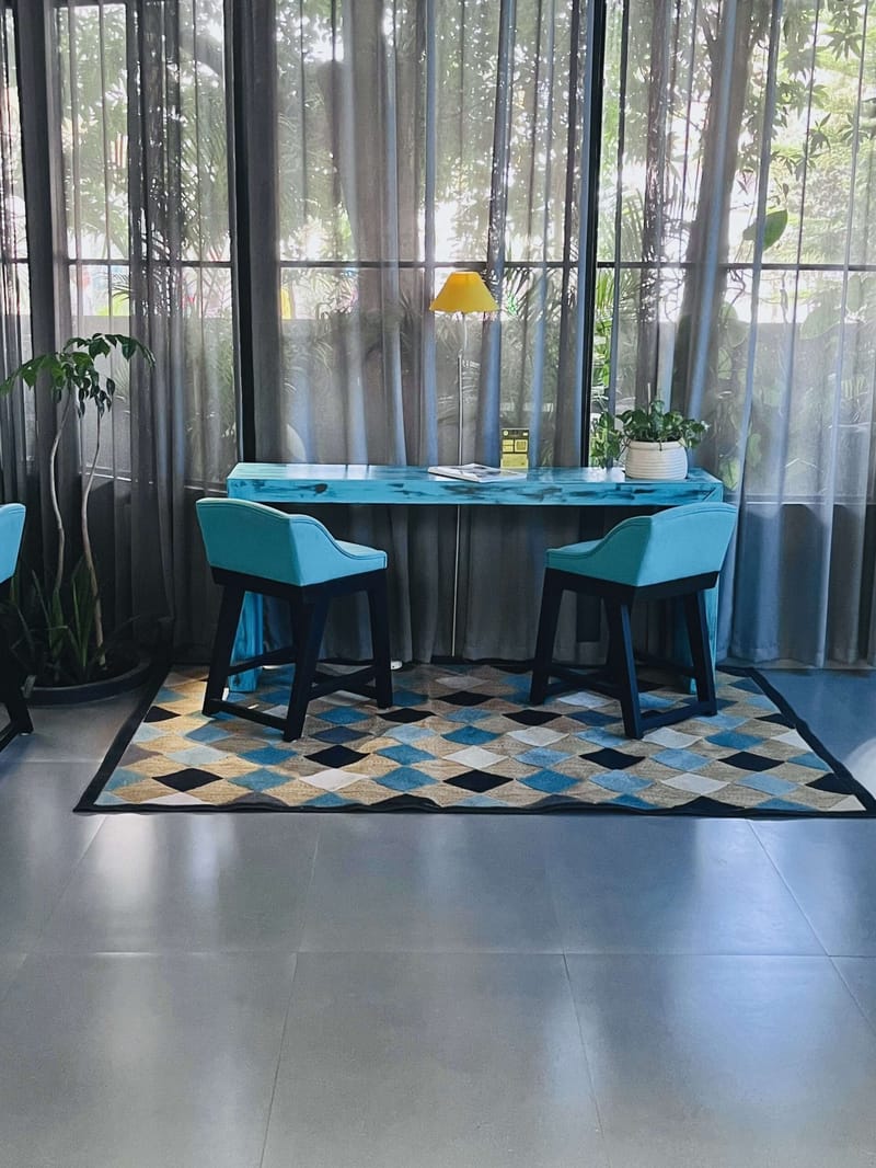 Breakfast nook with a turquoise table, teal chairs and a diamond-pattern rug beside sheer-curtained windows, Hyderabad