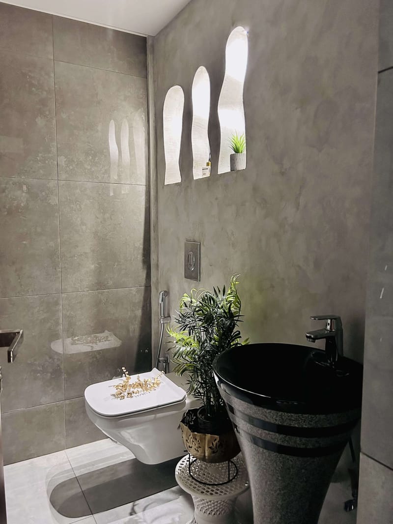 Entry lobby with potted palms, a white planter bed under a black steel staircase and stone-inlay floor, Hyderabad