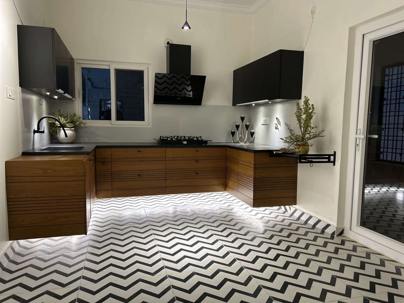 L-shaped kitchen with walnut and matte-black cabinets over bold black-and-white chevron floor tiles, Hyderabad
