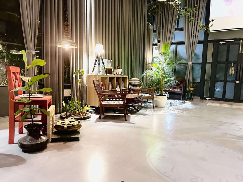 Double-height apartment lounge with floor-to-ceiling grey drapes, red accent stool, teak seating and potted palms, Hyderabad