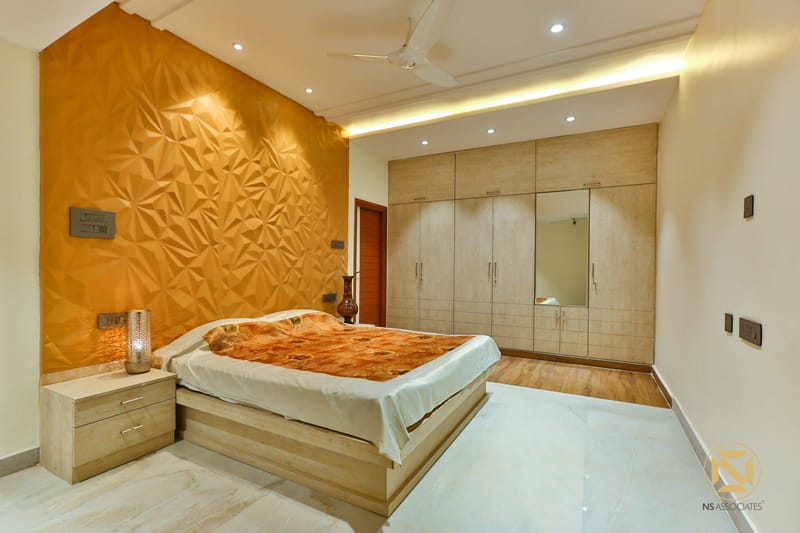 Bedroom with gold faceted accent wall, mirrored wooden wardrobe and amber bedside lamps, Hyderabad