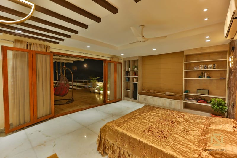 Bedroom with built-in wood wall unit, open display shelving and gold bedspread, doors opening to a night balcony in Hyderabad