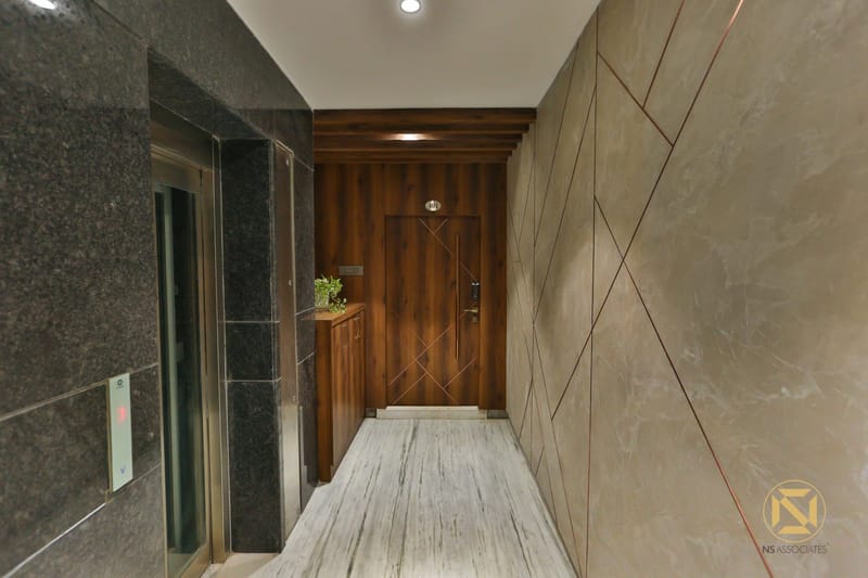 Entrance lobby with grey marble walls, slatted wood-panelled door and stone-look flooring under recessed lights, Hyderabad