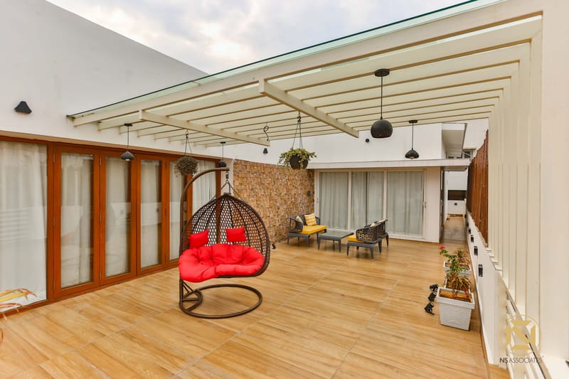Rooftop terrace lounge with red cushioned swing chair, wood-look tile flooring and pergola shade, Hyderabad