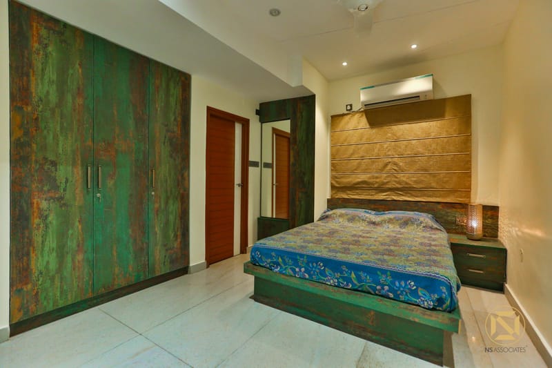Bedroom with rustic distressed green wardrobe, gold tufted headboard and floral blue bedspread, Hyderabad home