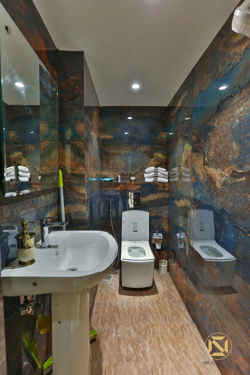 Bathroom clad in dramatic blue-and-rust marble with white pedestal basin and twin WCs over stone-look flooring, Hyderabad