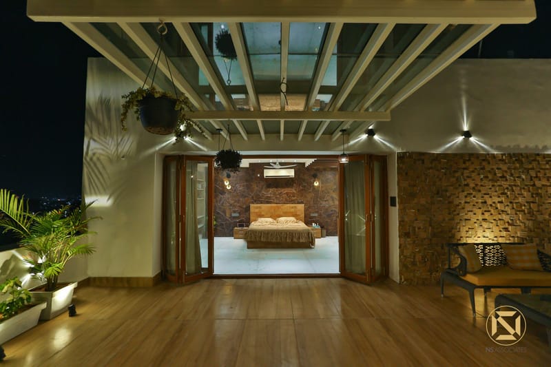 Wooden deck terrace under a pergola looking through glass doors to a brick-walled bedroom at night, Hyderabad full home