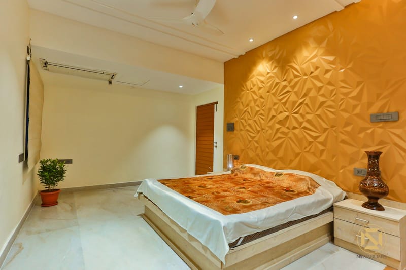 Bedroom with saffron 3D-textured accent wall, low wooden bed, floral spread and marble flooring, Hyderabad