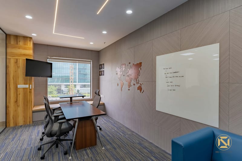Meeting room with wooden world-map wall art, glass whiteboard, wall-mounted TV and a dark conference table by a window, Hyderabad