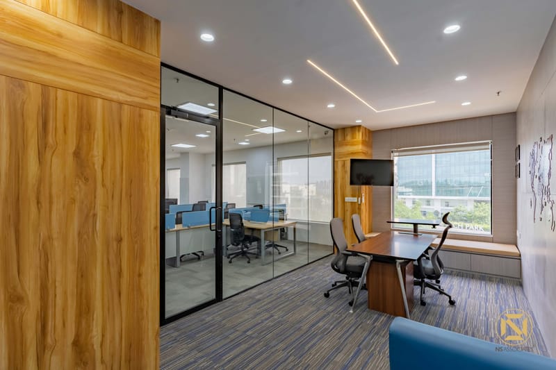 Glass-walled cabin with wood feature wall, mounted TV and window seat overlooking workstations, Hyderabad