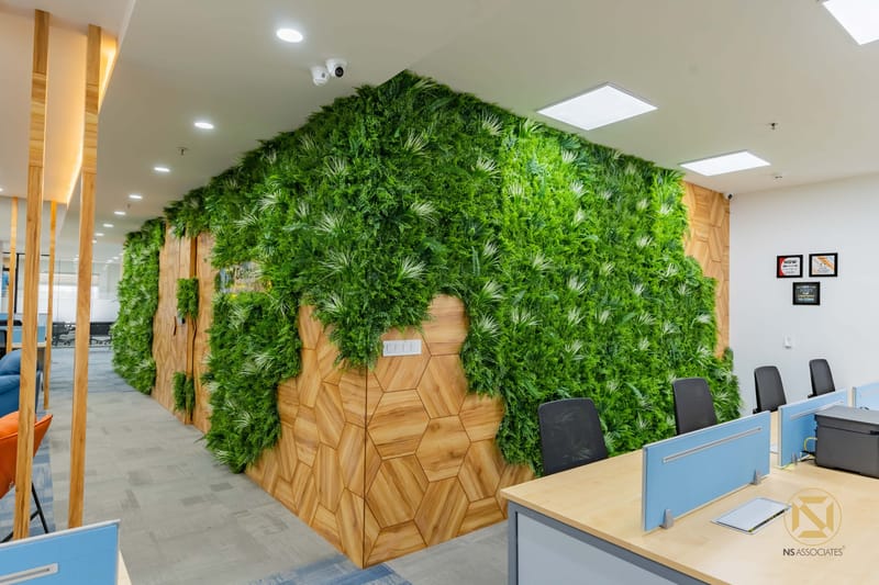 Office interior with lush green vertical garden over hexagonal wood panels and blue desk workstations, Hyderabad