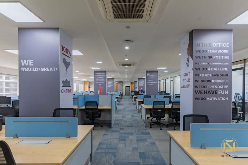 Open workspace with motivational printed pillars reading We Build Great and Teamwork above desks and blue dividers, Hyderabad