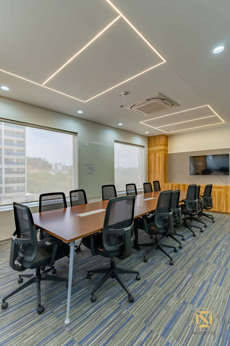 Conference room with long wooden table, black ergonomic chairs, linear LED ceiling lights, whiteboard and city view, Hyderabad