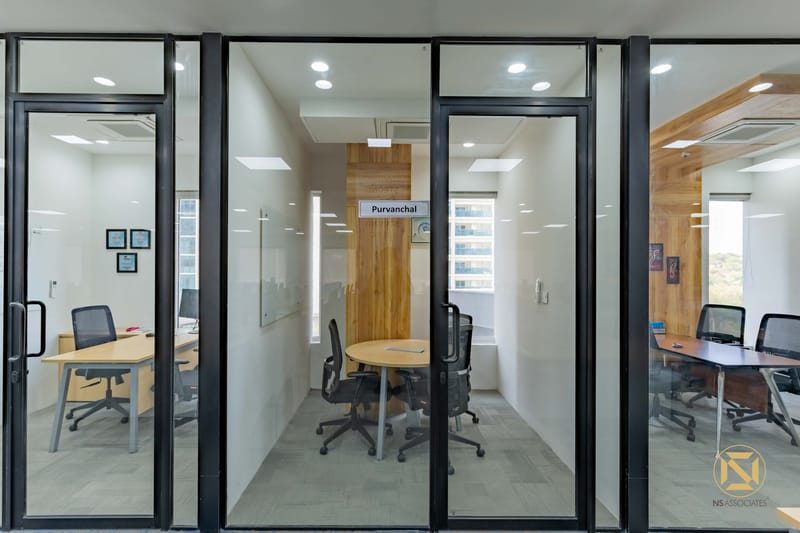 Corporate office cabins with black-framed glass partitions, wood accent wall and a round meeting table, Hyderabad