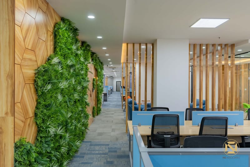 Open-plan office with green moss wall, wooden slat partitions, carpet tiles and rows of blue desks, Hyderabad