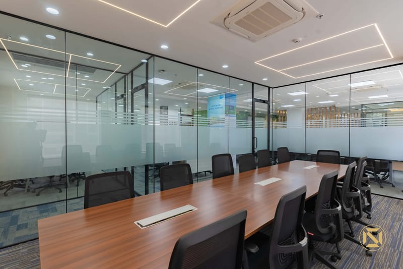 Boardroom enclosed in frosted glass partitions with wood-veneer table, black chairs and recessed cove lighting, Hyderabad