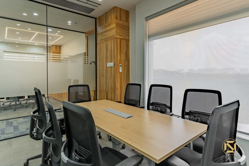 Glass-walled meeting room with wood-veneer table, black mesh chairs, wall display and frosted glazing, Hyderabad