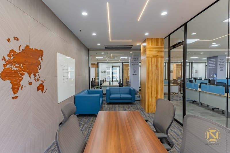 Breakout meeting area with carved wooden world-map wall art, whiteboard, blue armchairs and glass partitions, Hyderabad