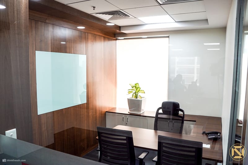 Small office cabin with wood-panelled wall, glass writing board, desk and black chairs, Hyderabad workplace