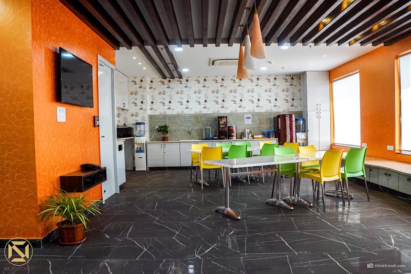 Office cafeteria with bright green and yellow chairs, orange accent walls, wood-slat ceiling and dark marble floor, Hyderabad