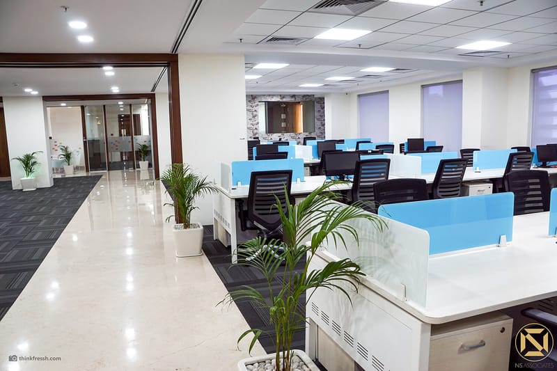 Open-plan office floor with blue-screened workstations, potted palms and polished tile aisle, Hyderabad workplace