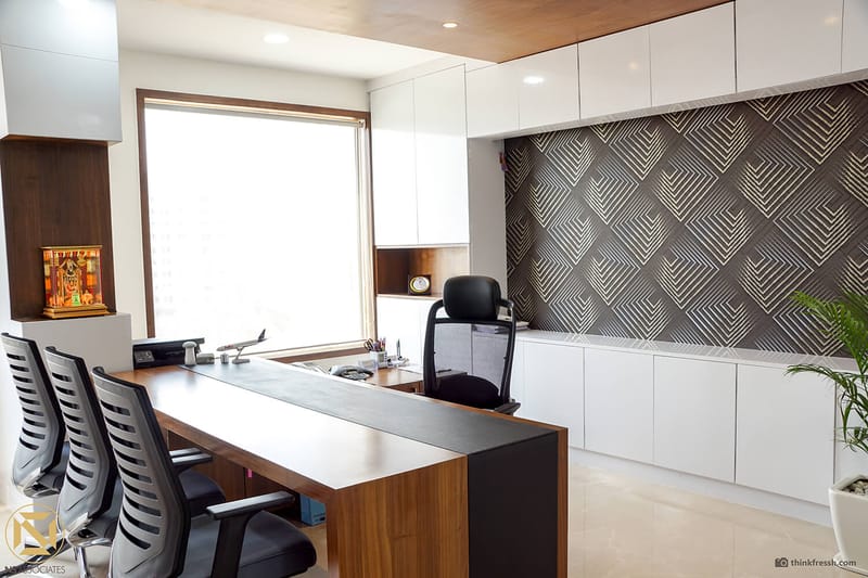Executive cabin in Hyderabad with wood-and-laptop desk, black chairs and patterned charcoal-and-gold accent wall