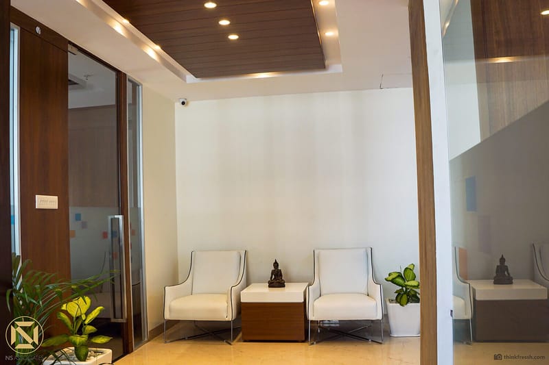 Office waiting lounge with two white armchairs, Buddha figurines and frosted-glass partition, Hyderabad workplace