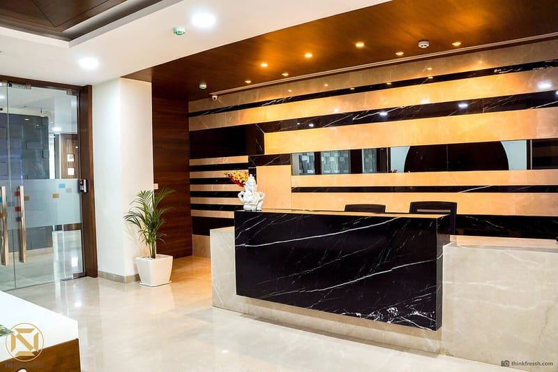 Reception desk in black-and-white marble against a backlit wood-and-tile wall in a Hyderabad corporate office