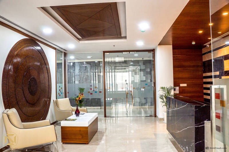 Corporate office reception in Hyderabad with carved wood medallion wall, cream leather chairs and black marble desk