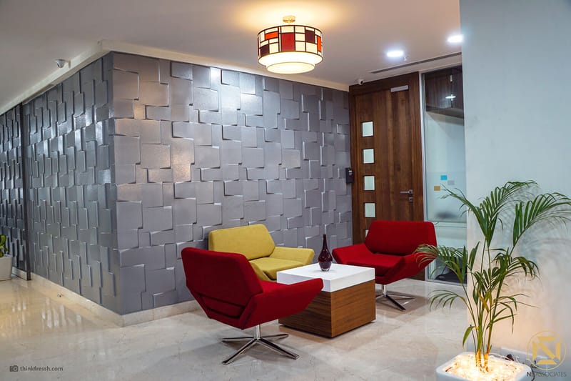 Office reception lobby with black marble desk, textured 3D-tile feature wall and red and yellow lounge chairs, Hyderabad