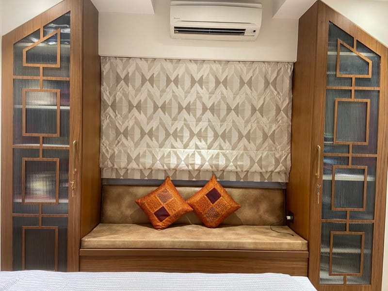 Cushioned window-seat alcove flanked by wood-and-glass fretwork panels under a geometric blind, Hyderabad bedroom