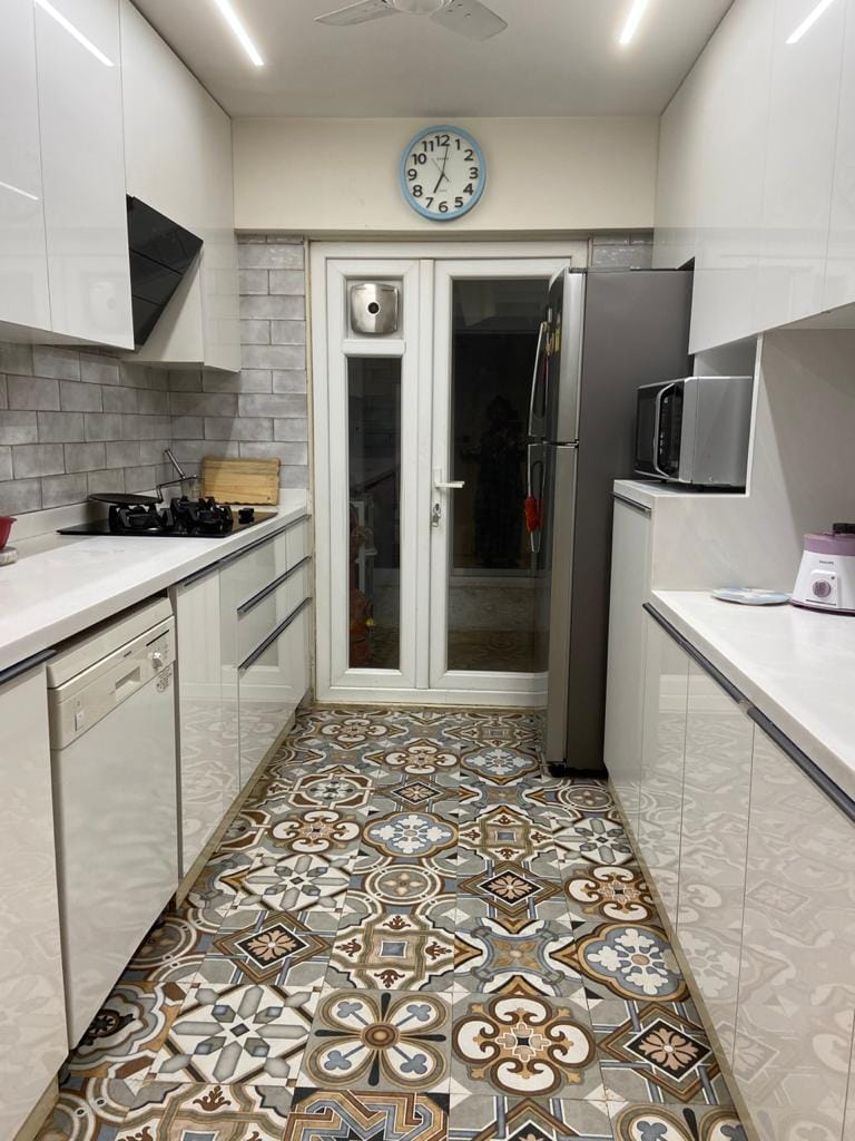 Galley kitchen with white handle-less cabinets, grey subway backsplash, steel fridge and ornate cement-tile flooring, Hyderabad