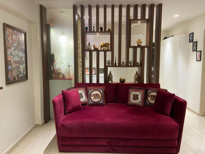 Living corner in Hyderabad with maroon velvet sofa, embroidered cushions and slatted wood display partition