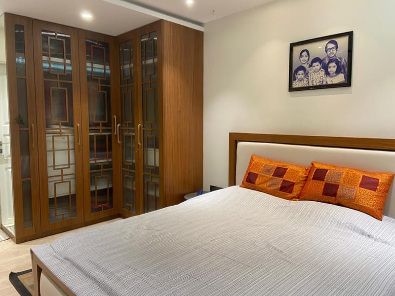 Bedroom corner with tall wood fretwork-and-glass wardrobes, upholstered headboard and orange patchwork pillows, Hyderabad