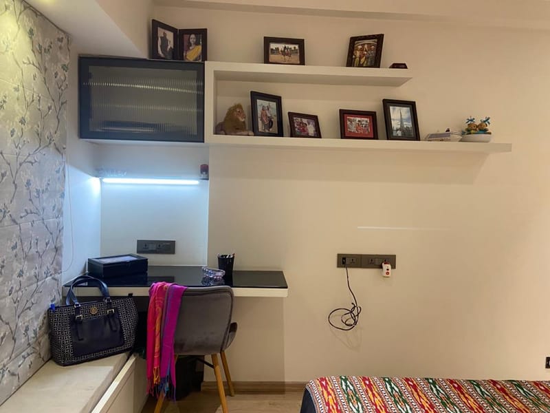 Bedroom study corner in Hyderabad with floating white desk, grey chair, framed photo shelf and floral wallpaper
