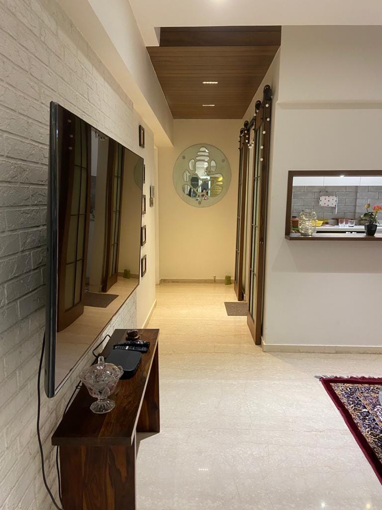 Hallway with whitewashed brick TV wall, wood-slat ceiling, round mirror and dark wood console, Hyderabad full-home interior