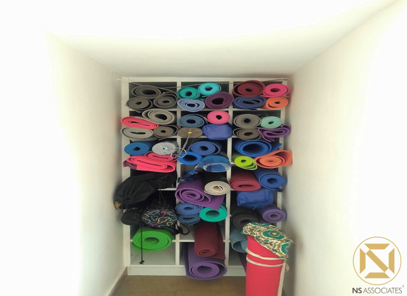 Yoga mat storage nook with white cubby shelving packed full of rolled colourful mats and bolsters, Hyderabad studio