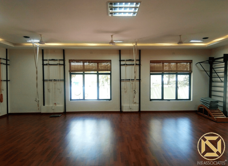 Yoga studio hall with polished dark wood floor, wall-mounted Iyengar rope props and bamboo blinds, Hyderabad