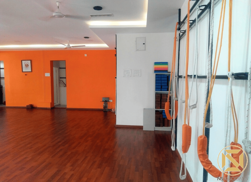 Yoga studio corner with orange wall, hanging practice ropes and stacked coloured mats, Hyderabad