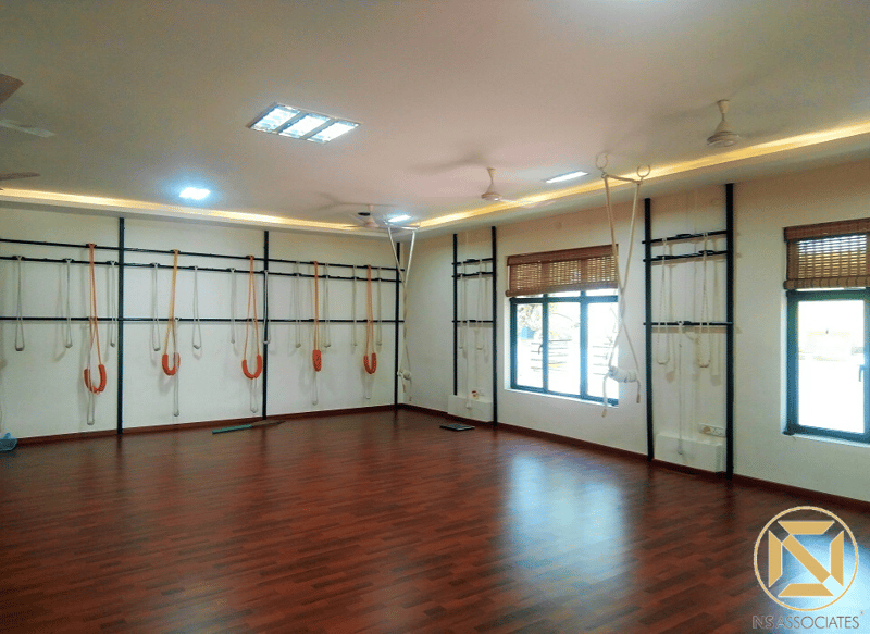 Iyengar yoga studio with rows of orange rope props on wall ladders, glossy wood flooring and bamboo-blind windows, Hyderabad