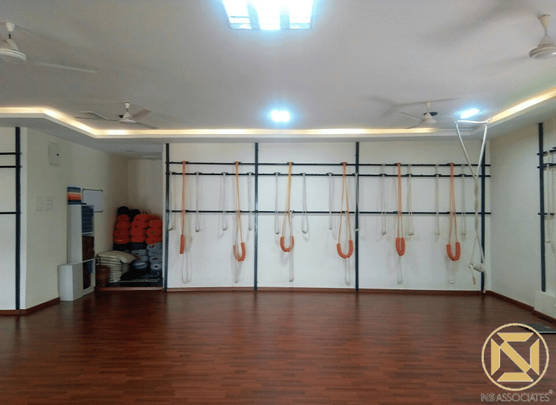 Iyengar yoga rope wall on white grid panels with prop storage over wood floor, Hyderabad studio
