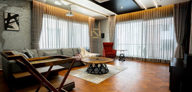 Spacious lounge wrapped in sheer curtains, grey sectional, red wingback chair and parquet flooring, Hyderabad