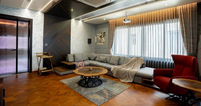 Living room with grey corner sectional, red accent recliner, live-edge coffee table and herringbone wood floor, Hyderabad