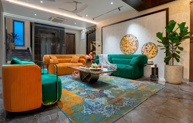 Bright living room in Hyderabad with emerald-green and ochre sofas, gold coffee table and a vibrant blue-orange patterned rug