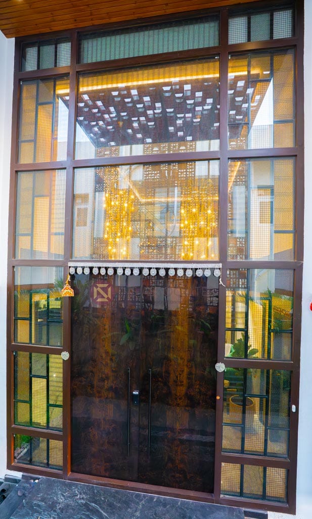 Glazed villa entrance with timber-framed glass facade, jali screen and warm fairy lights, Hyderabad