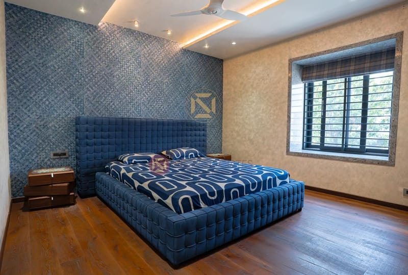 Bedroom featuring navy tufted bed, geometric blue accent wall and cove-lit false ceiling over wood floors, Hyderabad