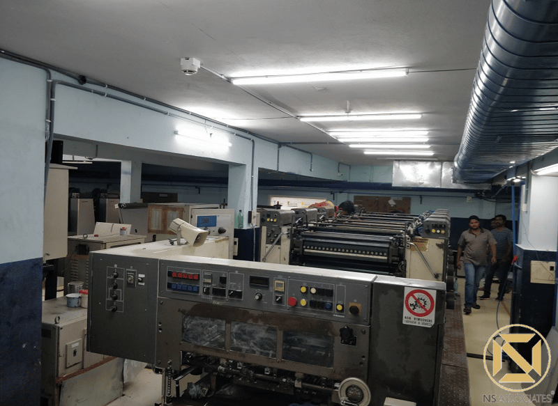 Offset printing press operating under tube lighting with ducting overhead, Hyderabad production floor