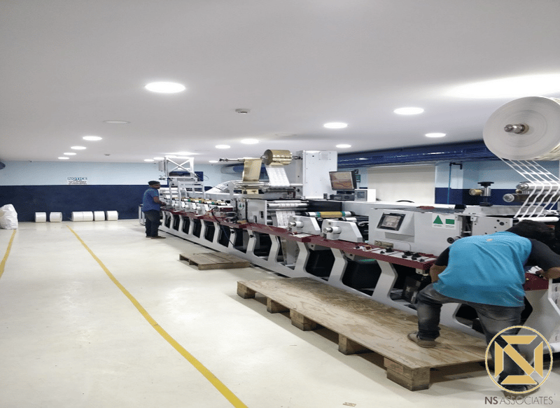 Industrial label-printing line with paper reels on a clean epoxy floor under bright lighting, Hyderabad plant